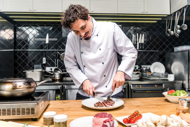 Professional chef slicing grilled steak on a plate in a commercial kitchen setting
